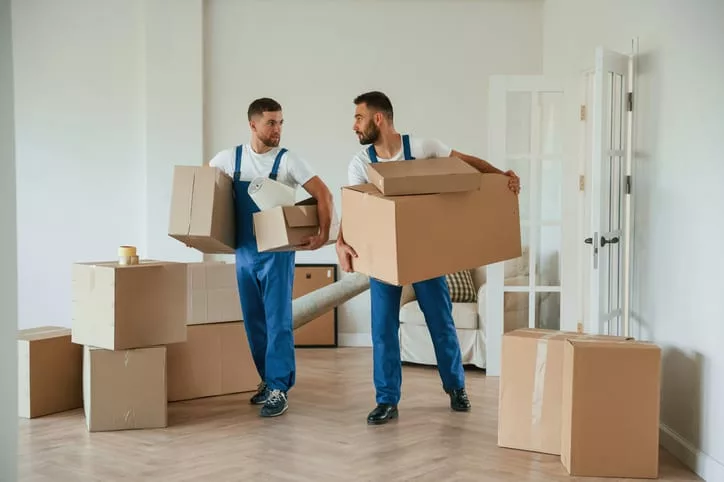 Due lavoratori di trasloco trasportano scatole in un appartamento, raffigurando servizi utili per utenti di self storage durante il trasloco - servizi di self storage