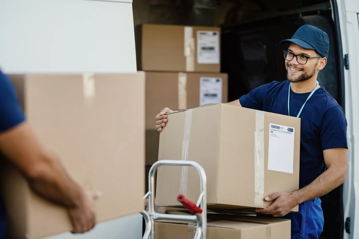 Happy manual worker unloading cardboard boxes from delivery van