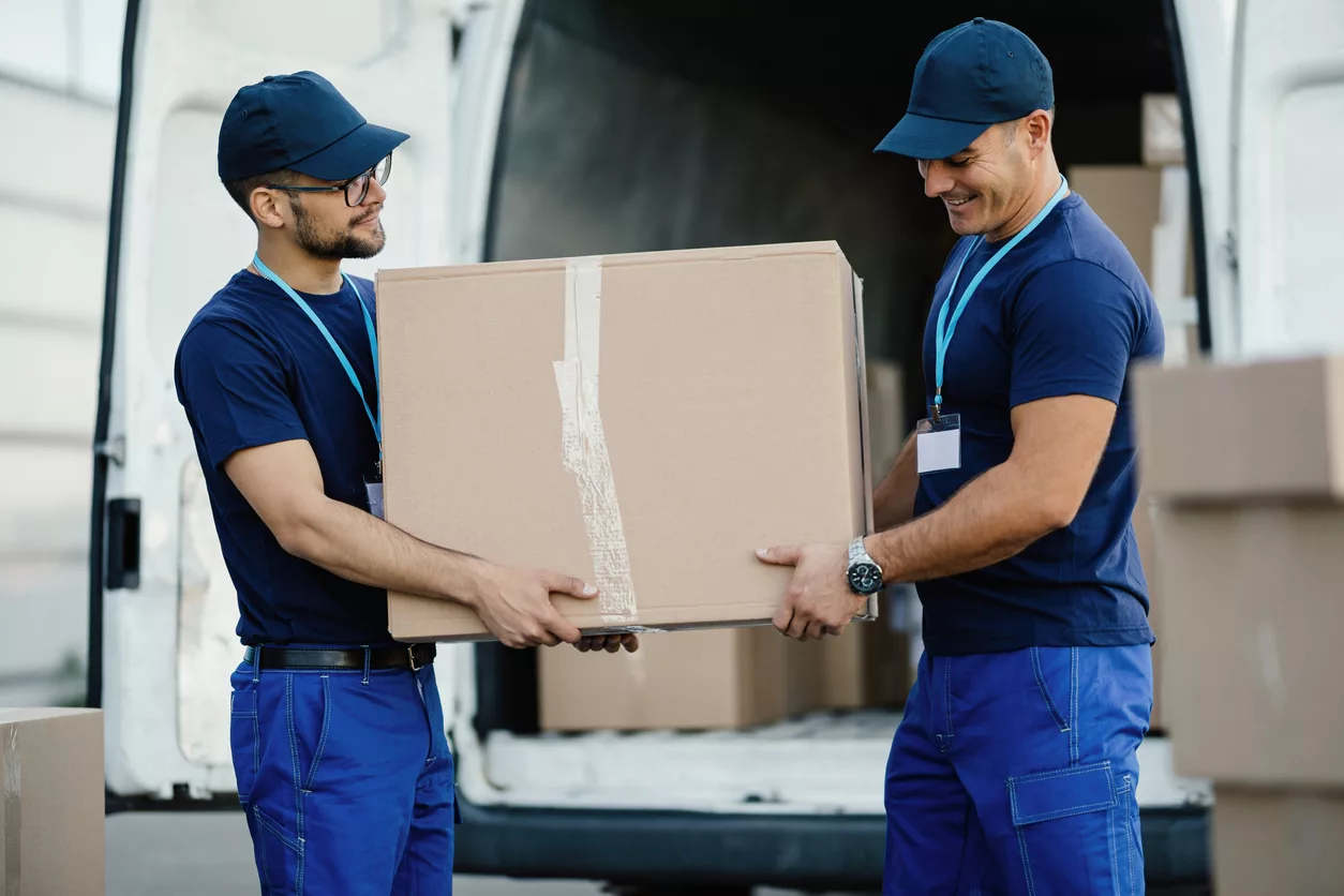 Manual workers carrying carboard box in a delivery van